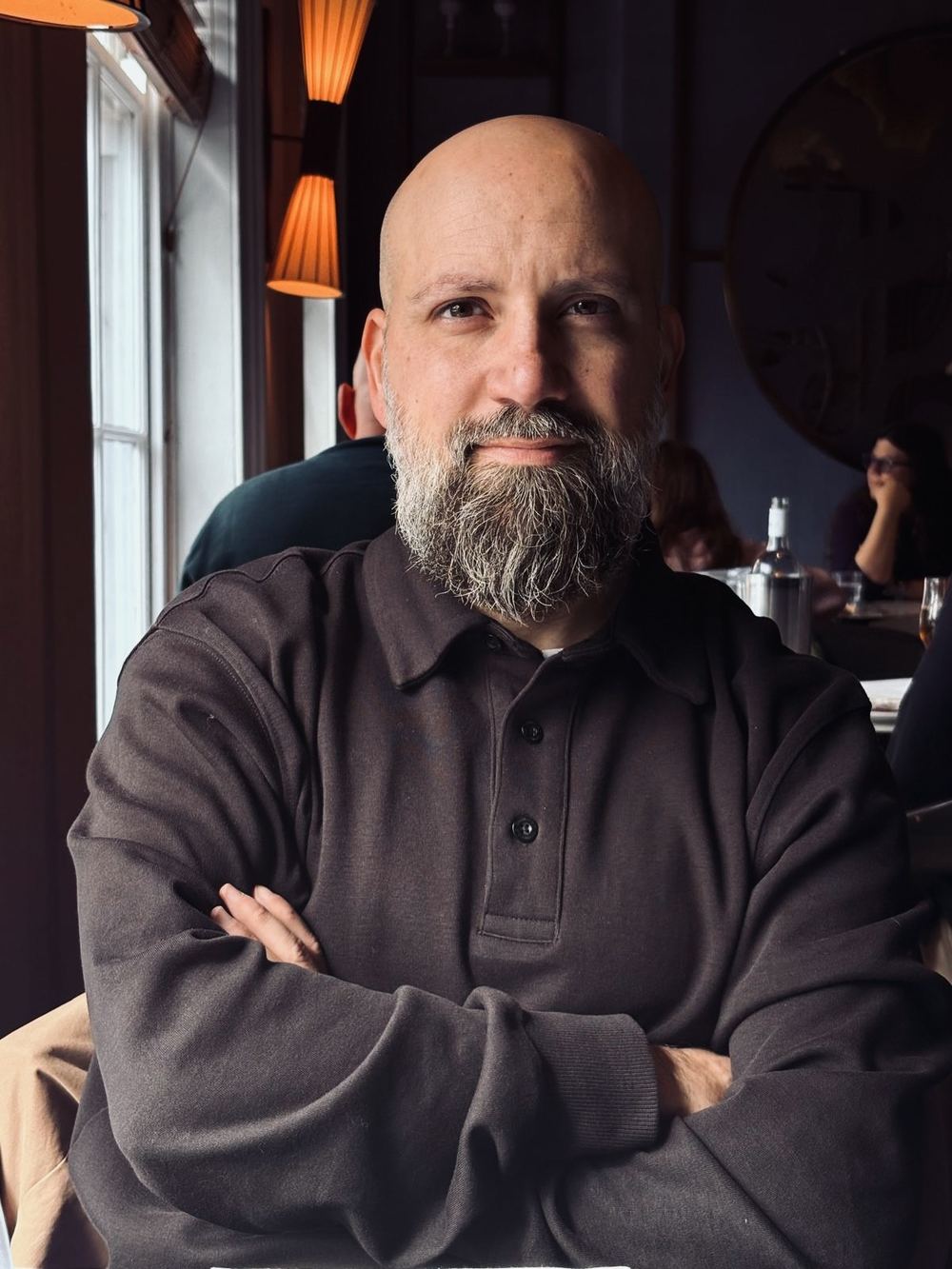 Sergio Aguado sitting at a restaurant table by a window, arms crossed