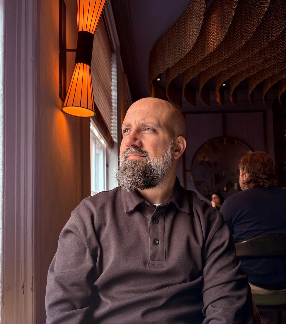 Sergio looking out of a window beside a warm amber lamp